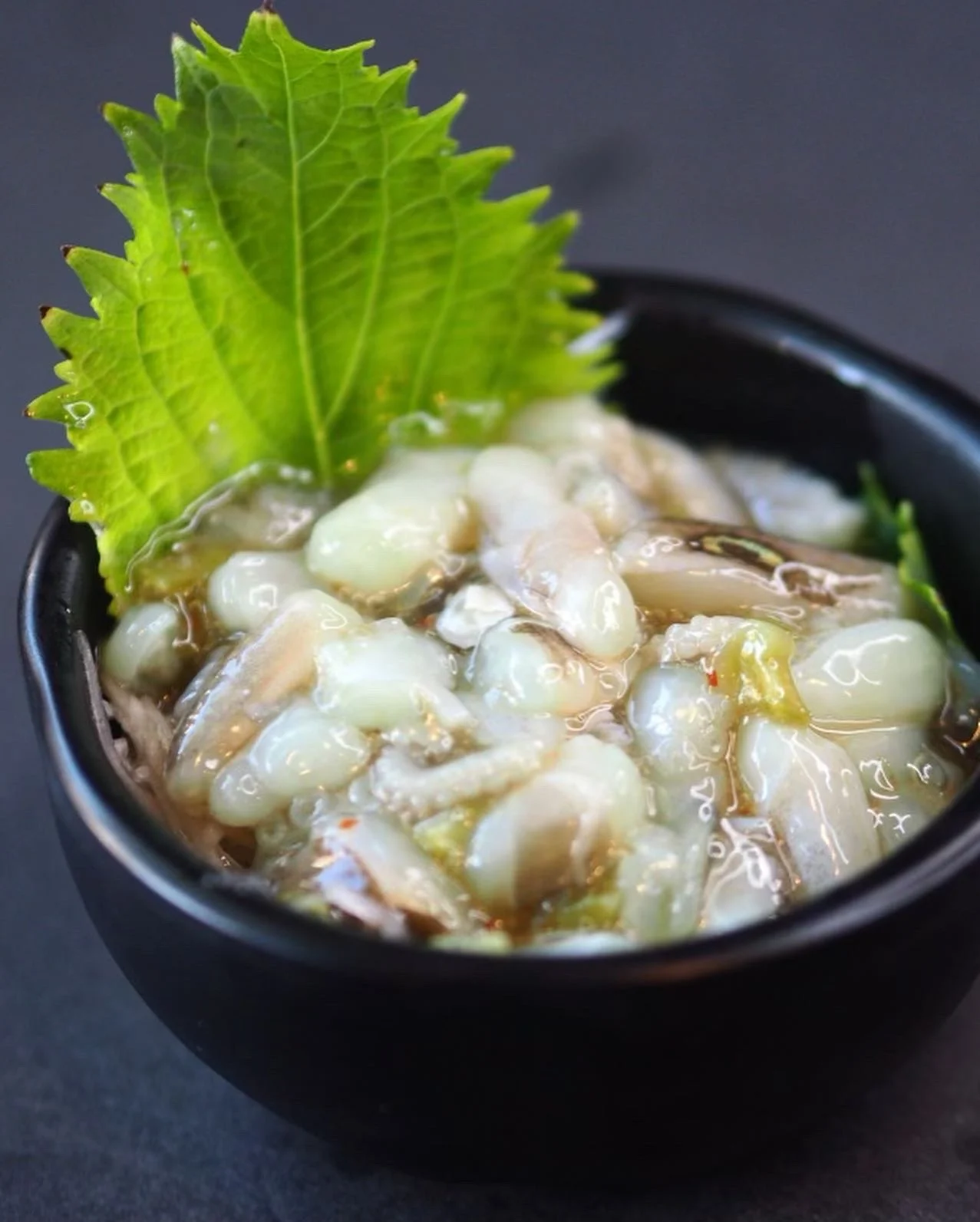 An octopus appetizer topped with a green shiso leaf in a small black bowl.