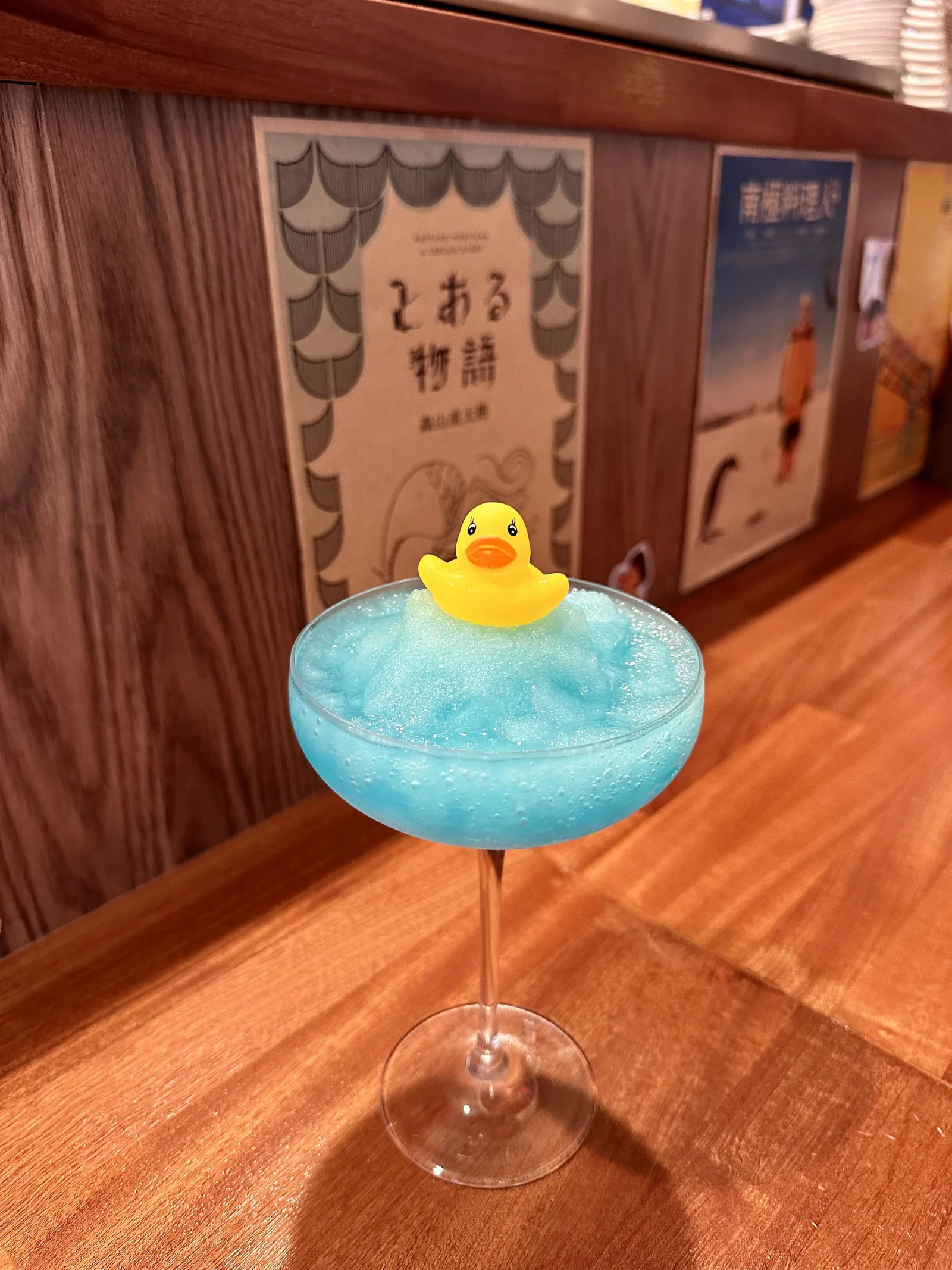 A blue frozen cocktail topped with a small yellow duck on Kinda’s wooden counter.