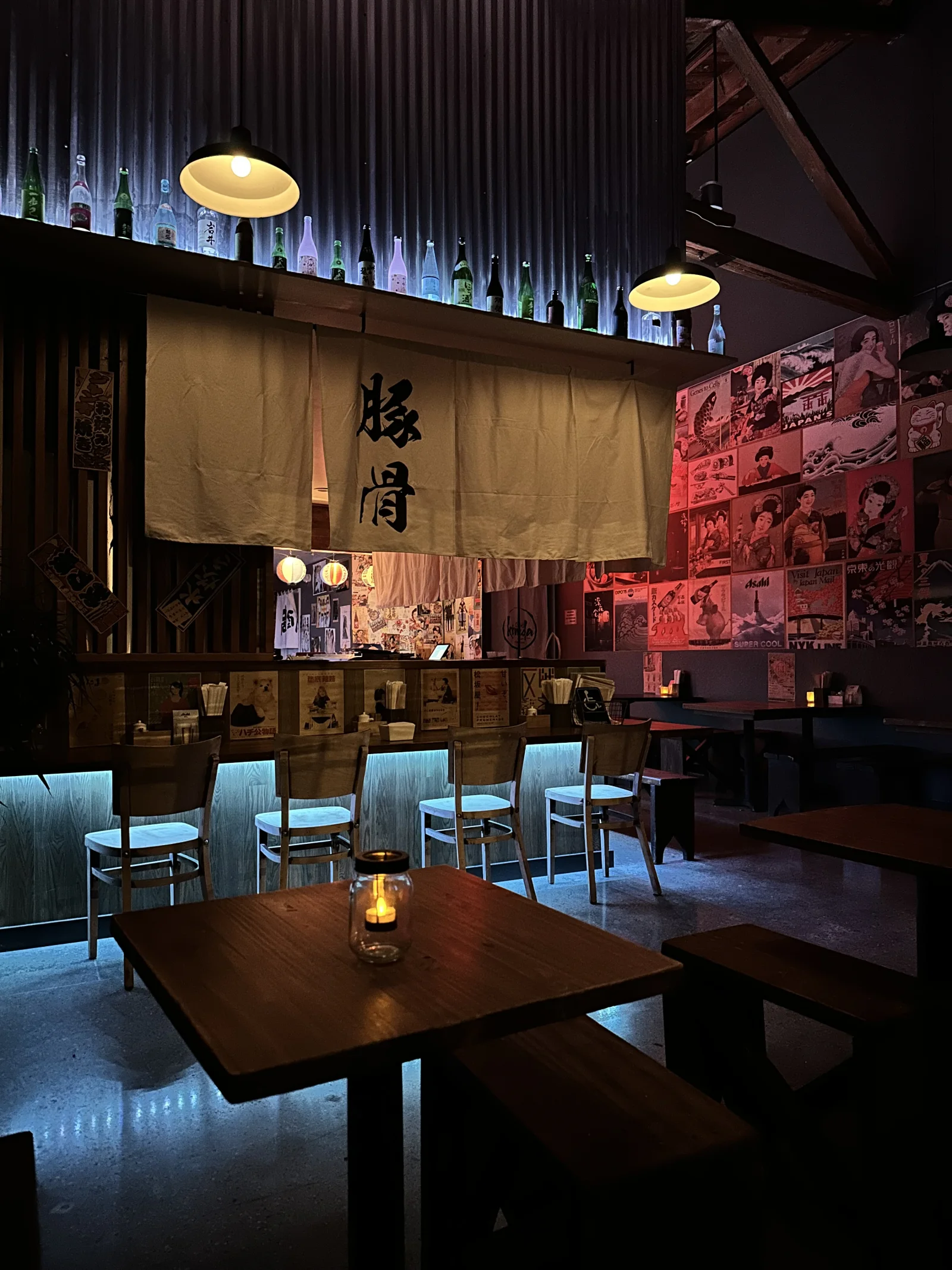 Kinda’s dim dining room with wooden tables, Japanese posters, hanging lamps and blue lighting along the floor.
